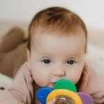 Bebê deitado brincando com mordedor colorido, representando conforto, segurança e bem-estar ao usar os melhores produtos para bebê.